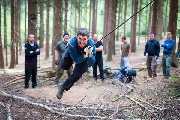 Mann überquert selbstgebaute Seilbrücke zwischen Bäumen im Wald