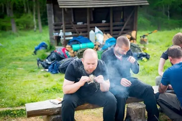 Mann zündet Zunder auf einer Holzbank an, Rauch steigt auf