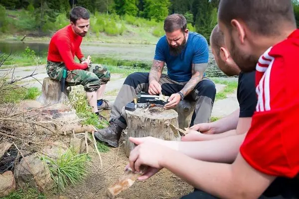 Mann zündet Zunder mit Feuerstahl auf Baumstumpf am Wasser