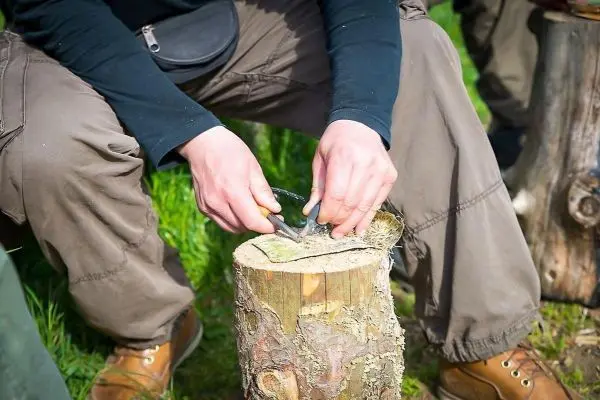 Messer schneidet Rinde von einem Holzstück auf dem Boden