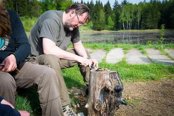 Messer schnitzt Holzstücke auf einem Baumstumpf am Ufer eines Gewässers