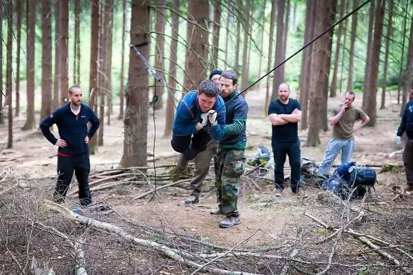 Person schwingt an einer selbstgebauten Seilbrücke, andere beobachten