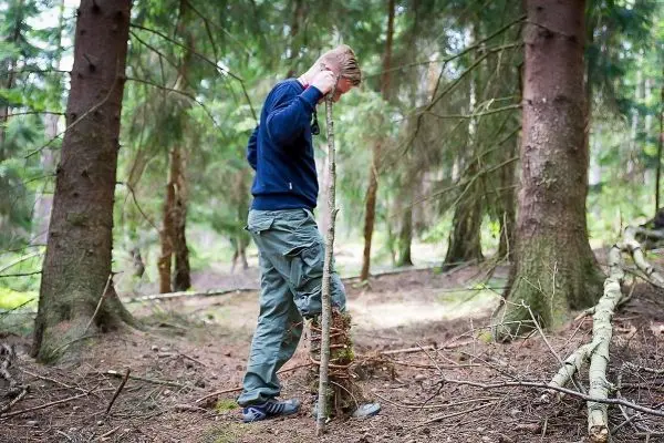 Person steht neben einer selbstgebauten Konstruktion aus Ästen im Wald