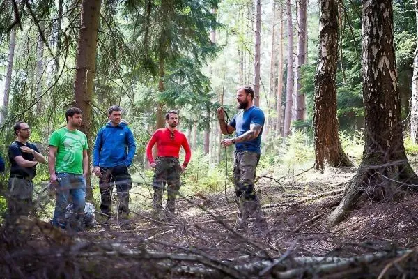 Person zeigt Gruppe von Männern eine Technik im Wald beim Survival Training
