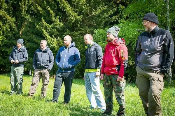 Sechs Personen stehen in einer Wiese vor Bäumen und beobachten etwas