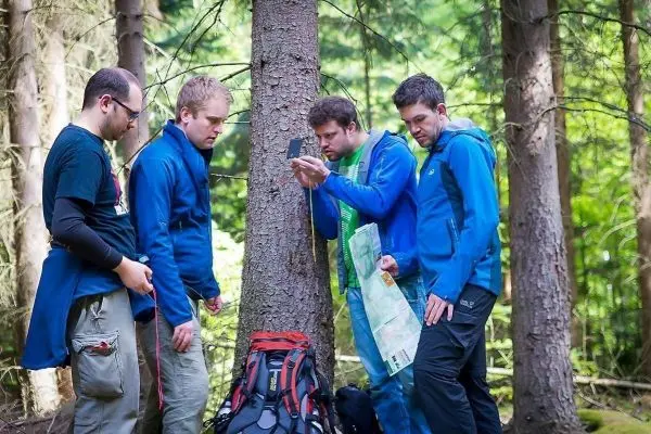 Vier Personen betrachten eine Karte und ein Gerät an einem Baum im Wald