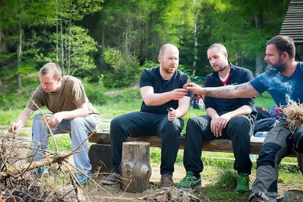 Vier Personen sitzen an einem Holzstamm und halten Zunder in der Hand