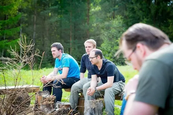 Vier Personen sitzen auf Baumstümpfen und beobachten eine kleine Feuerstelle