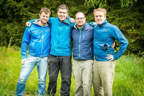 Vier Personen stehen nebeneinander in blauen Jacken auf einer Wiese