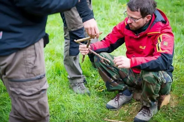 Zwei Personen arbeiten an einer selbstgebauten Schlagfalle aus Ästen
