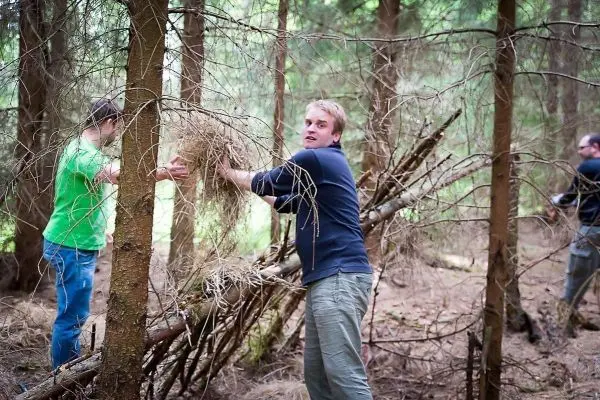 Zwei Personen bauen eine Notunterkunft aus Ästen und Zweigen im Wald