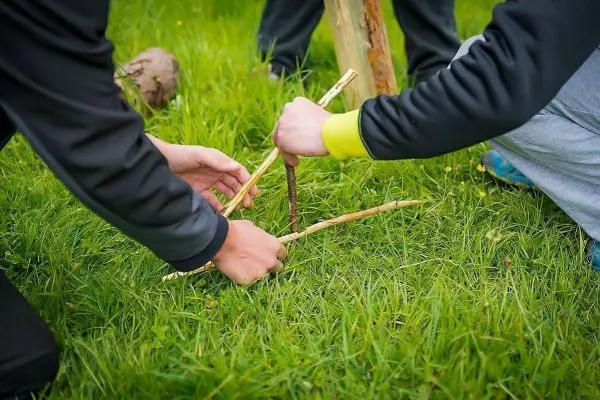 Zwei Personen bauen eine Struktur aus Ästen im Gras