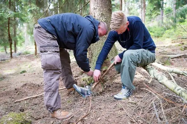 Zwei Personen bauen eine Struktur aus Ästen im Wald