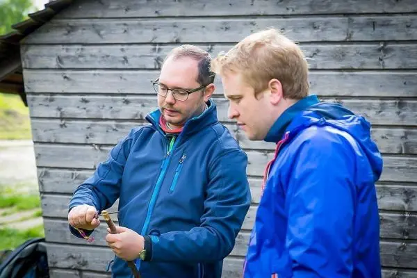 Zwei Personen betrachten ein Werkzeug vor einer Holzstruktur