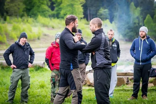 Zwei Personen demonstrieren eine Technik im Nahkampf, Zuschauer beobachten aufmerksam