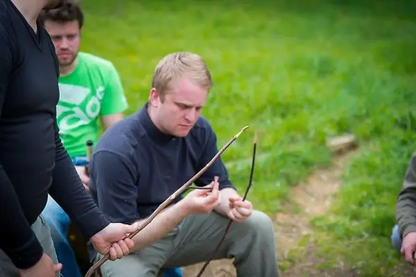 Zwei Personen halten Äste, während eine dritte Person aufmerksam schaut