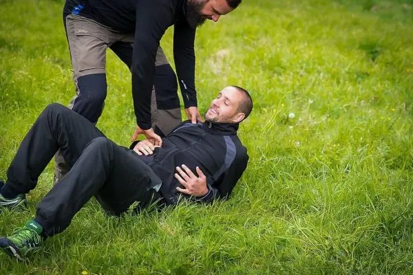 Zwei Personen helfen einem Mann, der auf dem Gras liegt