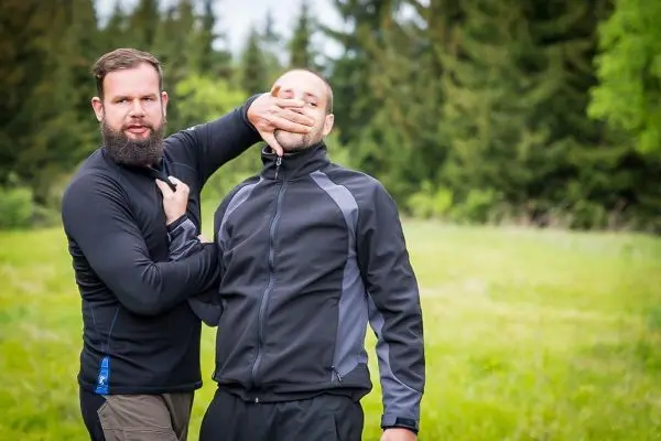 Zwei Personen in Outdoor-Bekleidung üben eine Selbstverteidigungstechnik im Freien