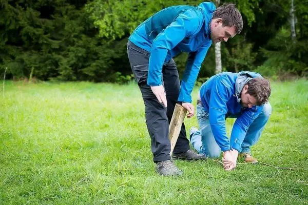 Zwei Personen positionieren einen Holzstock auf dem Boden
