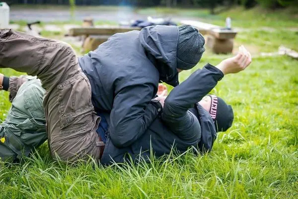 Zwei Personen ringen auf einer Wiese, eine liegt oben und hält die andere fest