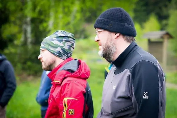 Zwei Personen stehen nebeneinander in der Natur, beide tragen wetterfeste Kleidung