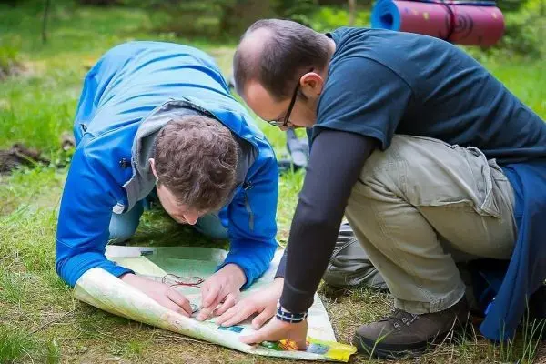 Zwei Personen studieren eine Karte auf dem Boden im Wald