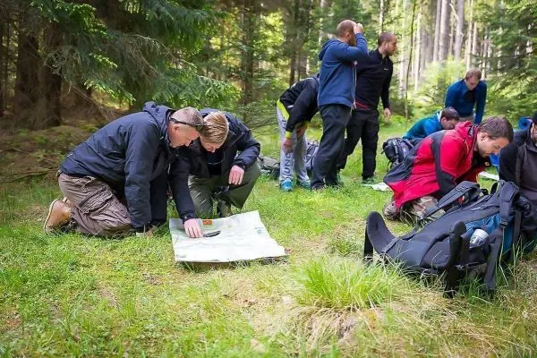 Zwei Personen studieren eine Karte auf dem Waldboden, weitere Teilnehmer im Hintergrund