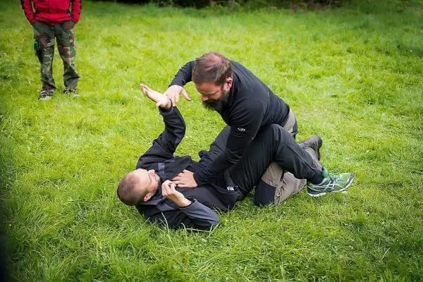 Zwei Personen üben eine Bodenkampftechnik auf einer Wiese