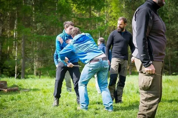 Zwei Personen üben eine Selbstverteidigungstechnik im Freien, während andere zuschauen