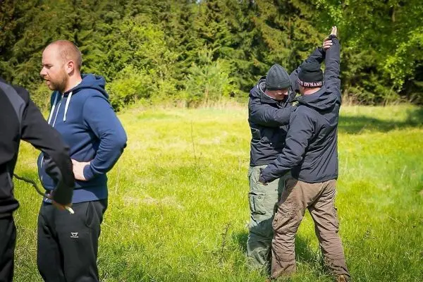 Zwei Personen üben eine Technik im Nahkampf auf einer Wiese
