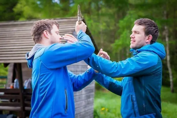 Zwei Personen üben eine Technik mit einem Holzstück in der Natur