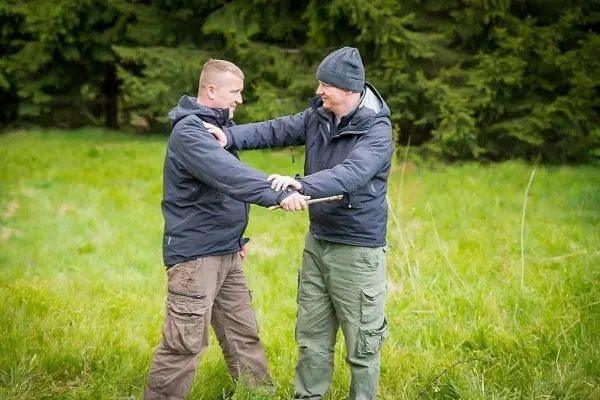 Zwei Personen üben eine Technik mit einem Stock in einer Wiese
