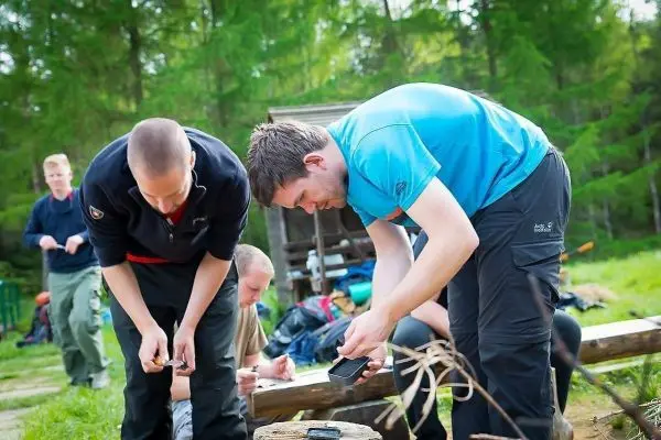 Zwei Personen überprüfen Ausrüstung auf einem Holzstamm im Freien