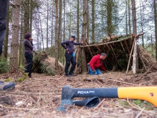 Drei Personen arbeiten an einer selbstgebauten Tarp-Notunterkunft im Wald