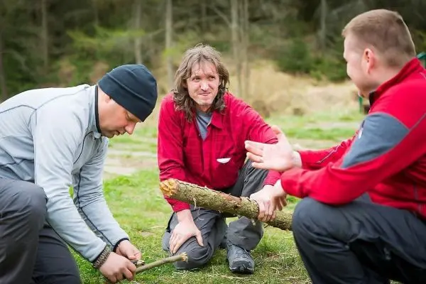 Drei Personen arbeiten gemeinsam an einem Holzstück im Freien