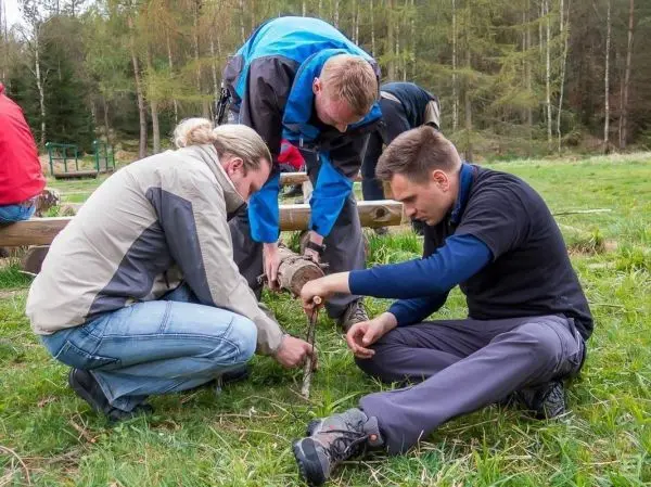 Drei Personen arbeiten gemeinsam an einem Holzstück im Freien