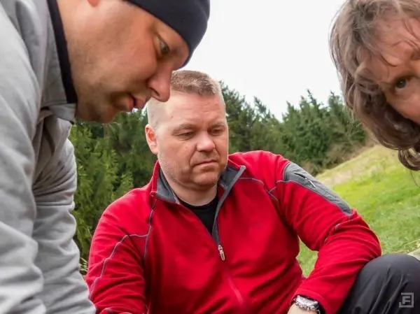 Drei Personen beugen sich über einen Bodenbereich in einer natürlichen Umgebung