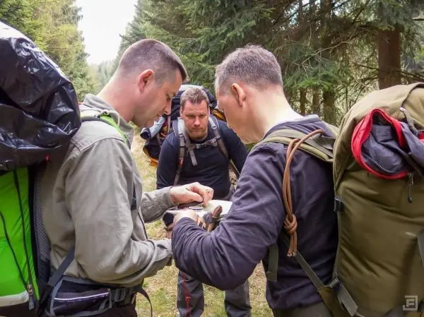 Drei Personen mit Rucksäcken betrachten eine Karte im Wald