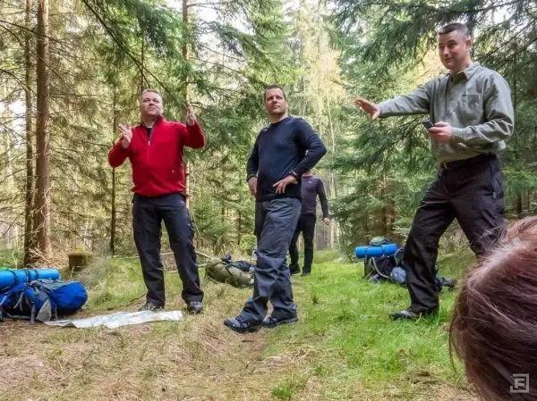 Drei Personen stehen im Wald und diskutieren über eine Karte auf dem Boden