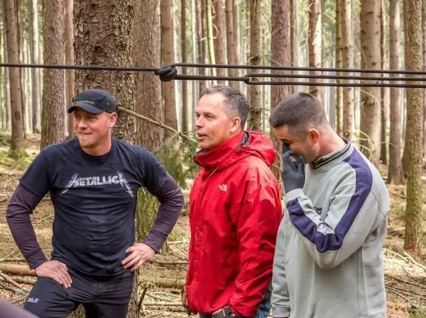 Drei Personen stehen im Wald und unterhalten sich, ein Seil ist gespannt