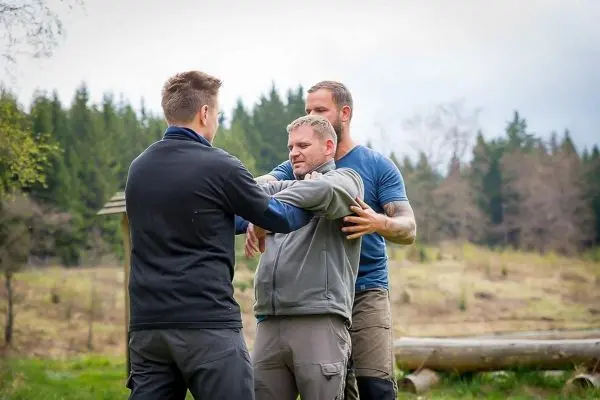 Drei Personen üben eine Technik zur Selbstverteidigung im Freien