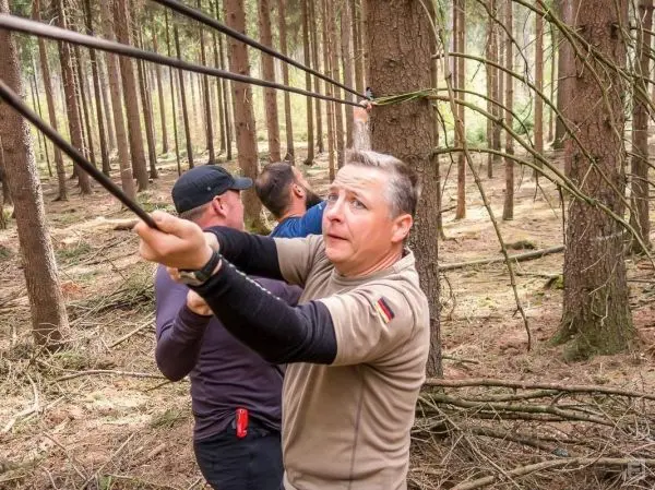 Drei Personen ziehen an einem Seil, das zwischen Bäumen gespannt ist