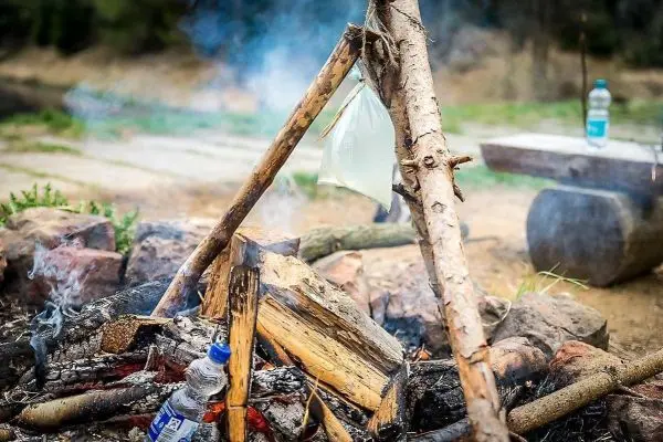 Ein Wasserbehälter hängt über einem Lagerfeuer aus Holz