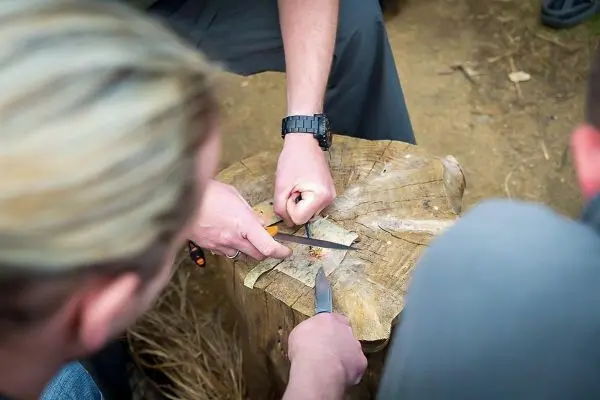 Feuerstahl erzeugt Funken auf Holzstück während Messer sichtbar ist