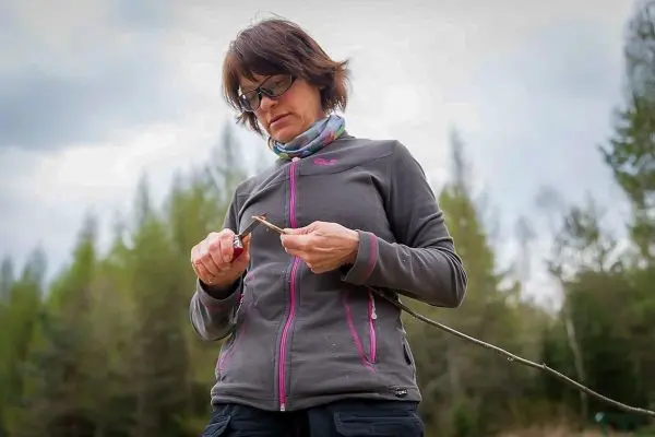 Frau bearbeitet einen Stock mit einem Messer im Freien