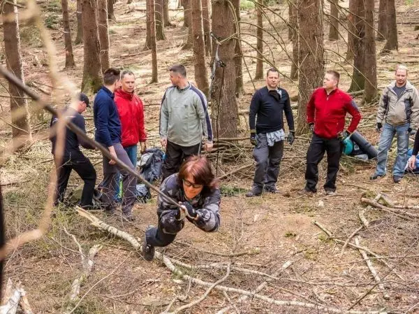 Frau überquert selbstgebaute Seilbrücke zwischen Bäumen, Gruppe beobachtet