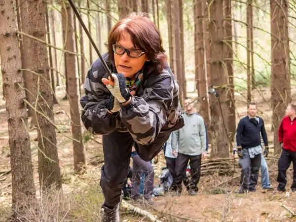 Frau überquert selbstgebaute Seilbrücke zwischen Bäumen im Wald