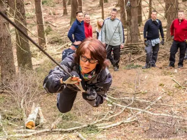 Frau überquert selbstgebaute Seilbrücke zwischen Bäumen im Wald