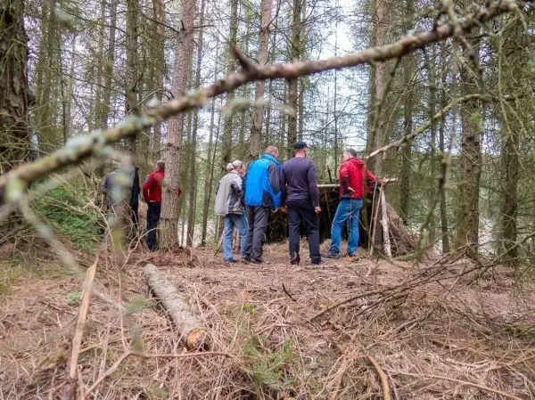 Gruppe arbeitet an einer selbstgebauten Tarp-Notunterkunft im Wald