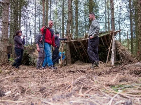 Gruppe baut eine Tarp-Notunterkunft aus Ästen und Laub im Wald